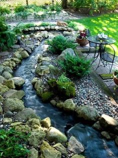 a small backyard with rocks and water running through the center, surrounded by greenery