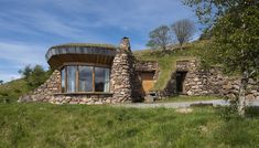 a stone house with a green roof and grass on the ground next to a hill