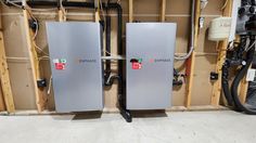 two silver refrigerators sitting next to each other in a room filled with wires and electrical equipment