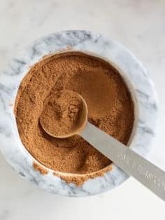 a bowl filled with cocoa powder and a spoon in the bowl next to it on a marble surface