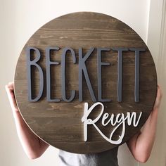 a person holding up a wooden sign that says beckett regn