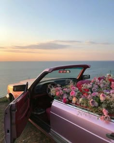 a pink car with flowers in the back door is parked near the ocean at sunset