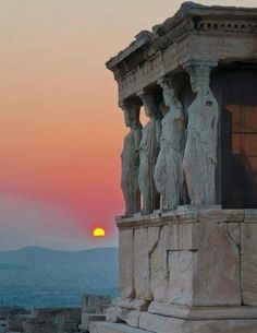 the sun is setting behind some statues on top of a building with mountains in the background