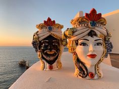 two masks are sitting on the roof of a building near the ocean, one is wearing a turban