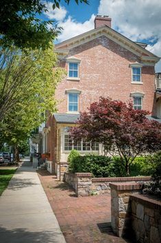 a brick building with trees and bushes on the sidewalk