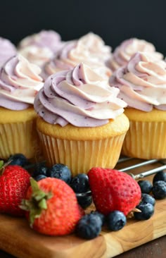 cupcakes with frosting and strawberries on a cutting board