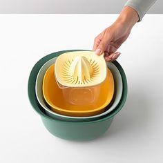 a person is holding a yellow and green bowl over three different colored bowls that are stacked on top of each other