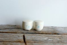 two white ceramic salt and pepper shakers sitting on top of a wooden table next to each other