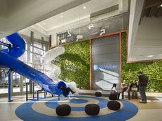 people are sitting in the lobby at an office building with a slide and climbing wall