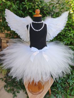 a mannequin with white tulle and pearls on it sitting in front of some bushes