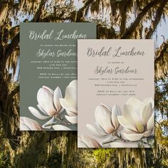 two wedding cards with white flowers and moss hanging from the tree branches in front of them