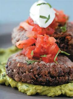 two burgers topped with tomatoes and guacamole on top of each other