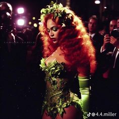 a woman with long red hair and green dress standing in front of a group of people