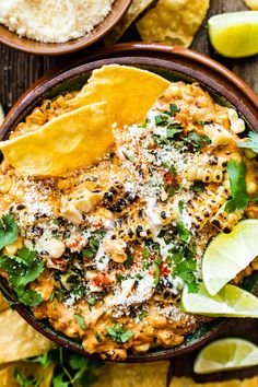 a bowl filled with mexican food surrounded by tortilla chips and lime wedges