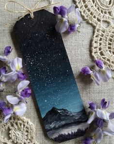 a bookmark with purple and white flowers next to it on a lace doily