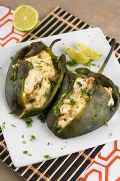 two stuffed peppers on a white plate with lemon wedges and garnishes