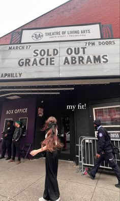 a woman walking down the street in front of a theater