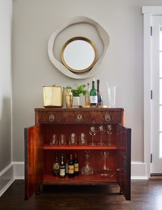 a cabinet with wine glasses and bottles on it in front of a round wall mirror