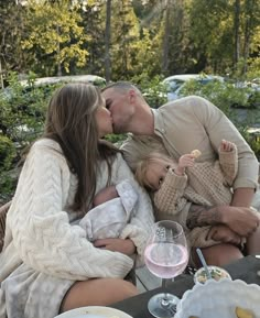 a man and woman kissing while holding a baby in front of a table full of food