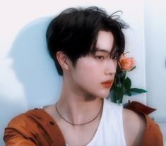 a man with black hair wearing a white tank top and holding a rose in his hand