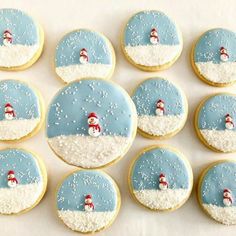 frosted cookies decorated with snowmen and santa hats are arranged on a white surface