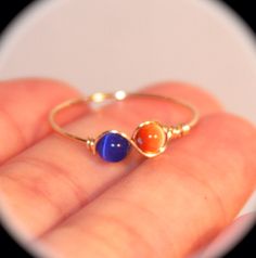 a hand holding a gold ring with two different colored stones on it's side