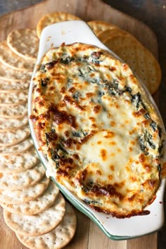 cheese and spinach dip in a casserole dish with crackers on the side