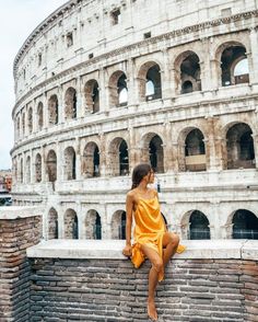 a woman in an orange dress sitting on a brick wall next to the colossion