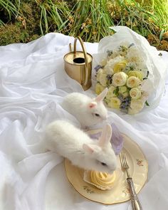 two white rabbits sitting on top of a plate next to a vase with flowers in it