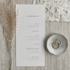 two gold wedding rings on top of a white menu card next to a silver plate