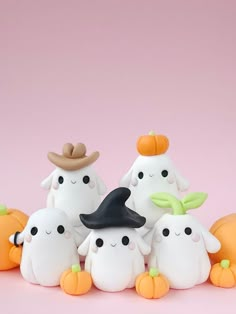 a group of small white ghost figurines with pumpkins on the ground in front of a pink background