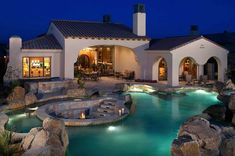 a house with a pool in front of it and rocks surrounding the pool area at night