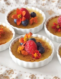 four small bowls filled with food on top of a white table covered in flowers and fruit