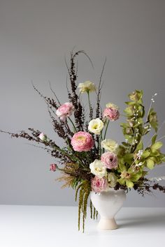 a white vase filled with lots of flowers on top of a table next to a gray wall