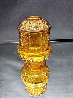 a yellow glass candle holder sitting on top of a reflective surface with its reflection in the water