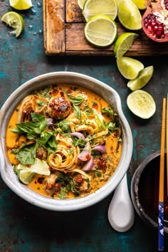 a bowl filled with noodles, meatballs and vegetables next to sliced limes on a cutting board