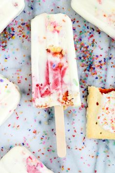 colorful sprinkles and ice cream popsicles on a marble surface with white frosting