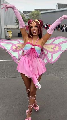 a woman dressed in pink and green is posing with her arms spread out, wearing a butterfly costume