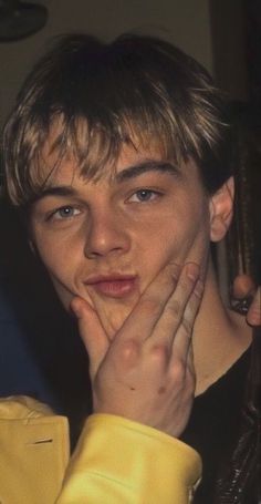 a young man with his hand on his face looking at the camera while wearing a yellow jacket