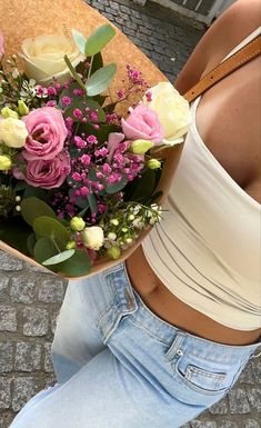 a woman holding a bouquet of flowers in her hand on the street with brick pavement