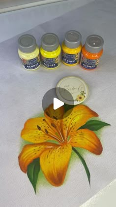 an orange flower is on the table next to some paint bottles and a white cloth