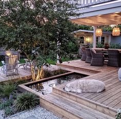 a dog laying on top of a wooden deck next to a small pond in the middle of a yard