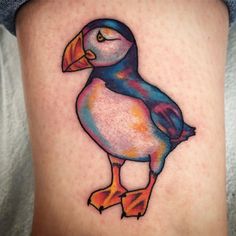 a colorful bird tattoo on the thigh