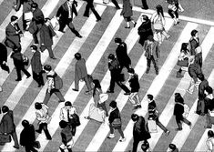 black and white image of people walking across a crosswalk in the city, from above