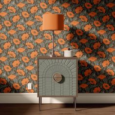 an orange flowered wallpaper is next to a cabinet with a lamp on it