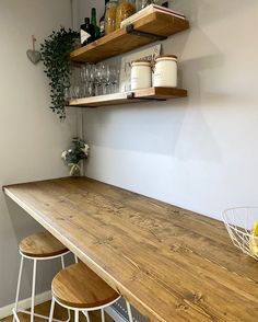 a kitchen counter with two wooden stools next to it and shelves on the wall