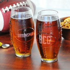 two beer glasses sitting on top of a wooden table next to a football and cereal bowl