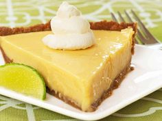 a slice of cheesecake on a plate with a fork and lime wedge next to it