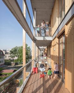 children are standing on the balcony of an apartment building with wooden floors and walls, while two adults look out onto the street