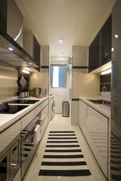 a long narrow kitchen with black and white striped rugs on the floor, along with stainless steel appliances